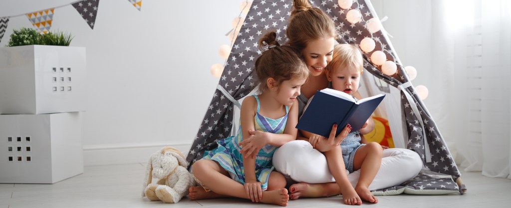 family mother reading to children book in tent at home